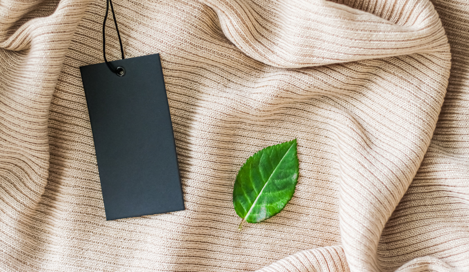 A blank clothing label and a green leaf atop a piece of woven fabric