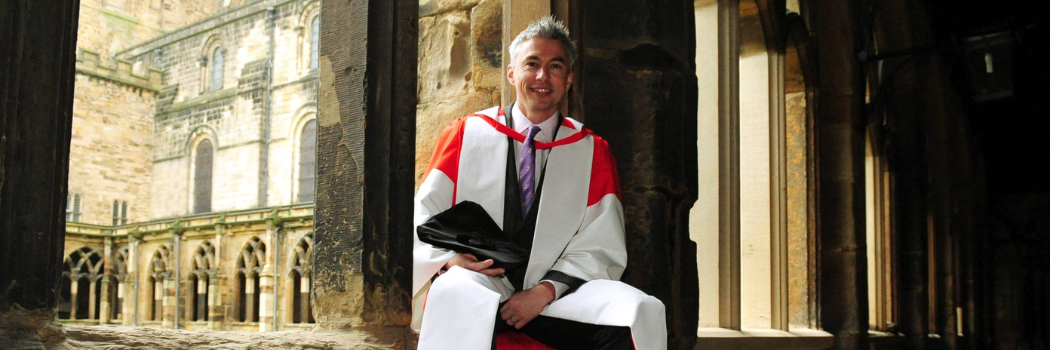 Alumnus Jonathan Edwards robed in Hon Grad robes, sitting in the Cloisters