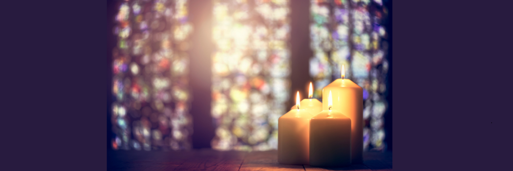 Four lit candles with stained glass window in the background.