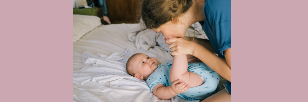 A mother kissing her baby's foot whils the baby is lying on the bed