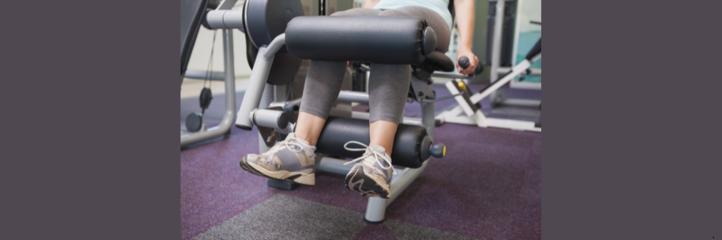 A person wearing trainers sitting on a weights machine.