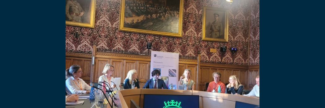 Panel of speakers sat at horseshoe shaped table in large room within the Houses of Parliament
