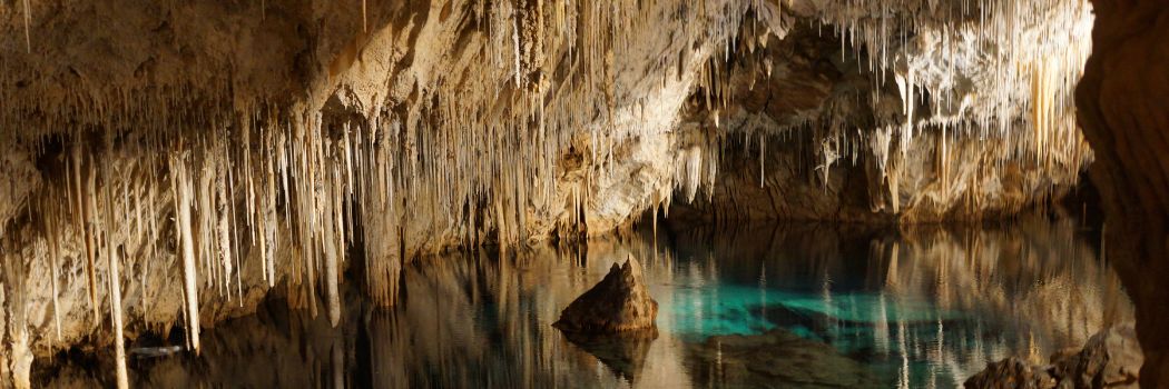 A cave with stalactites hanging from the ceiling being reflected in a pool of water beneath them.