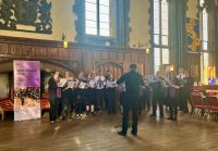 A group singing from sheet music in the Great Hall. Conductor in the foreground.