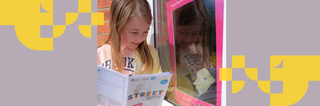A young girl with blonde hair reads a booklet with Street Museum written on the front