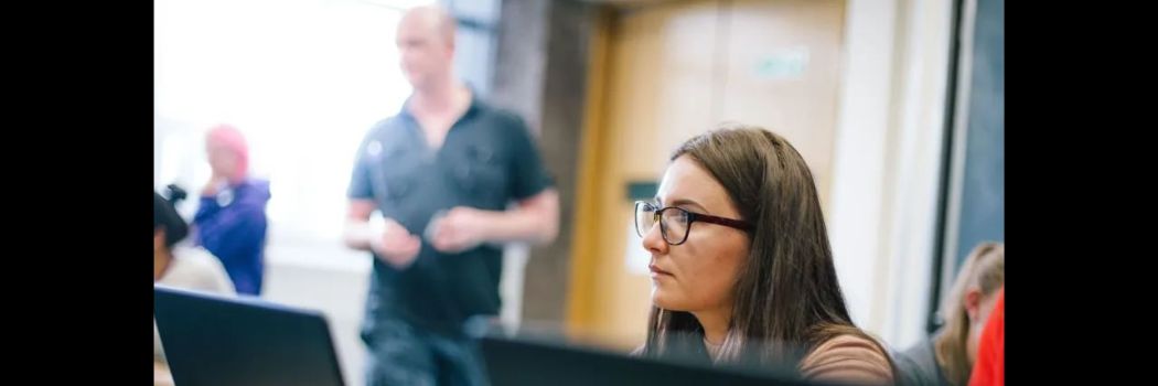 Person sitting at computer, other people at computers in background
