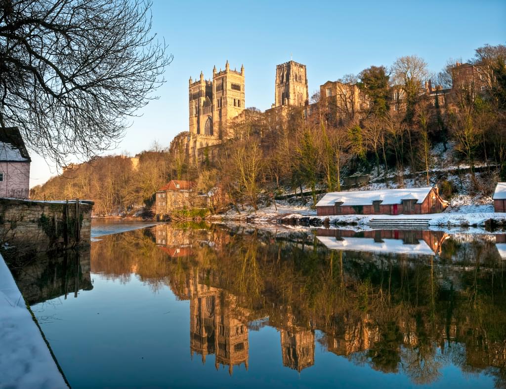 Photo of the River Wear and snowy banks on a winter's morning, with Durham Cathedral lit up by the sun and reflected in the water.