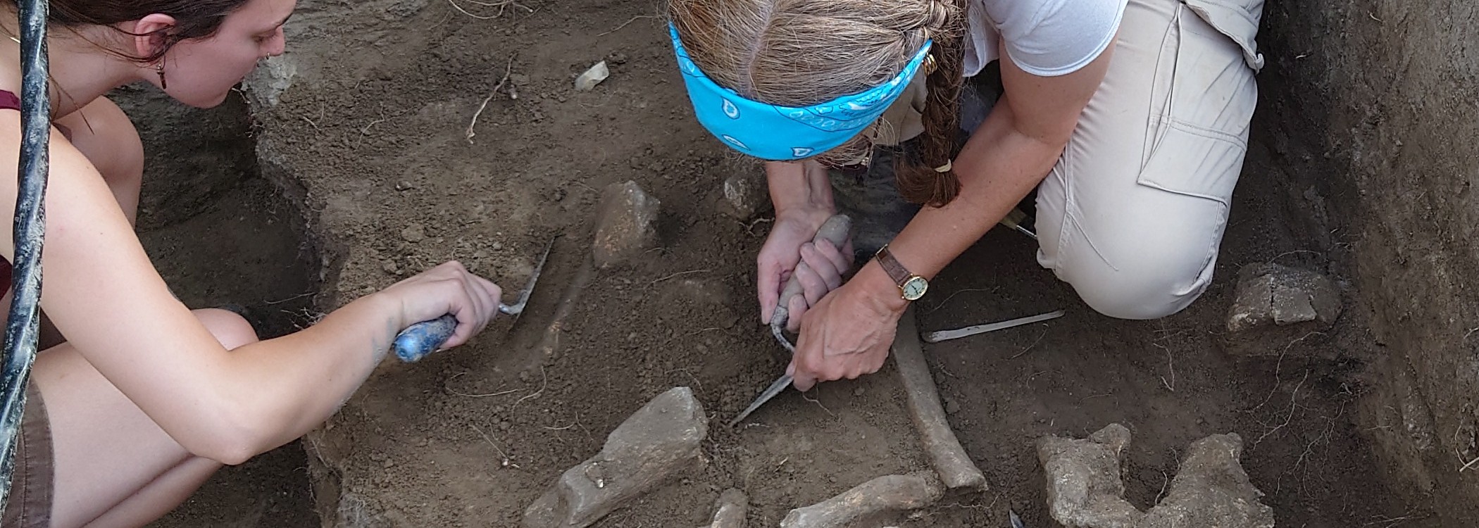 Two students crouch in an archaeological section excavating mammoth bones.
