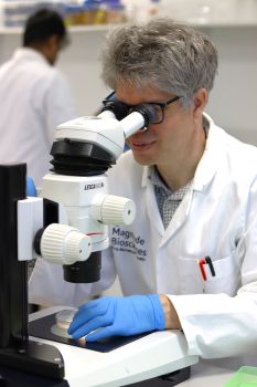 Man in white laboratory coat looking down a microscope