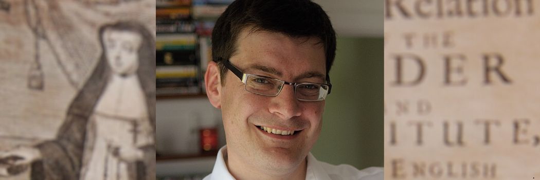 Headshot of a man with dark hair and wearing glasses.