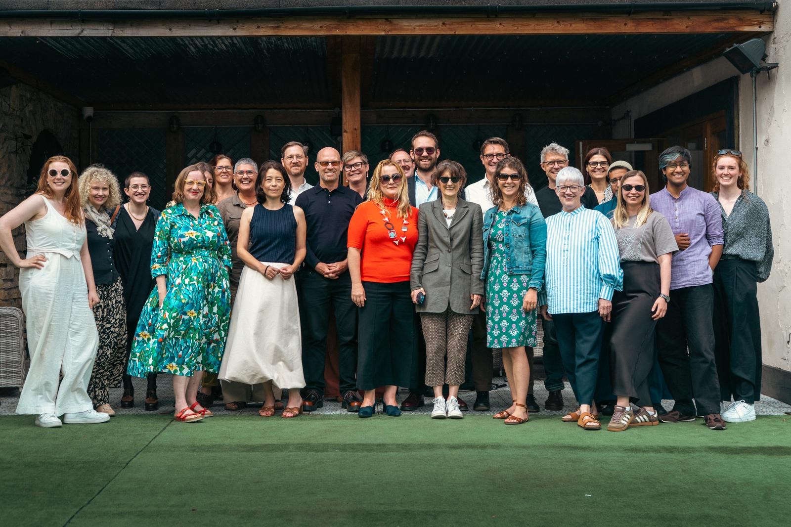 Photograph of a group of people in smart casual attire, standing on a grass patch and smiling at the camera.
