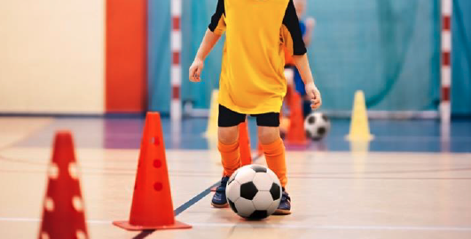 A child kicking a football at a holiday club in a school gymnasium