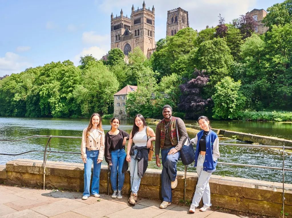 TStudents standing next to the riverside with the cathedral in the background