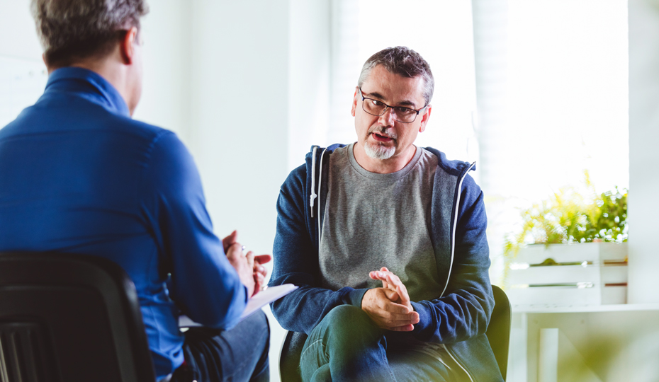 A psychotherapist discussing mental illness with a man. They are meeting in a psychotherapeutic office.