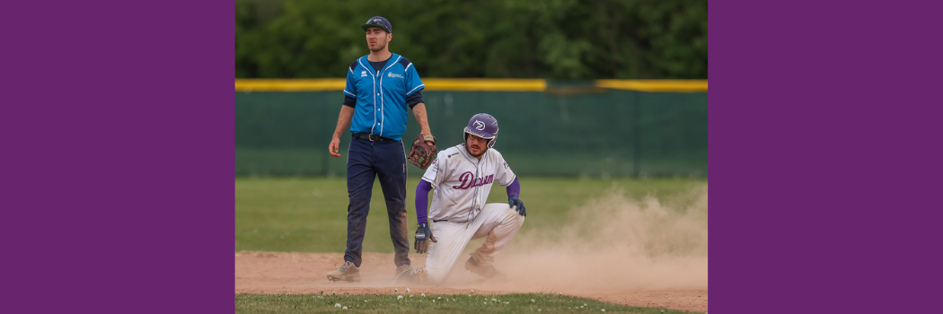 A Durham baseball player kneels at a base with a cloud of dust behind him.