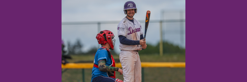 A Durham baseball player with a bat smiles at the catcher behind him.